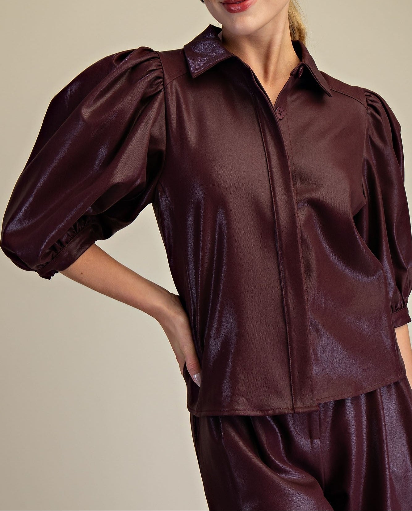 Woman wearing a burgundy faux leather blouse with puffed sleeves on a beige background