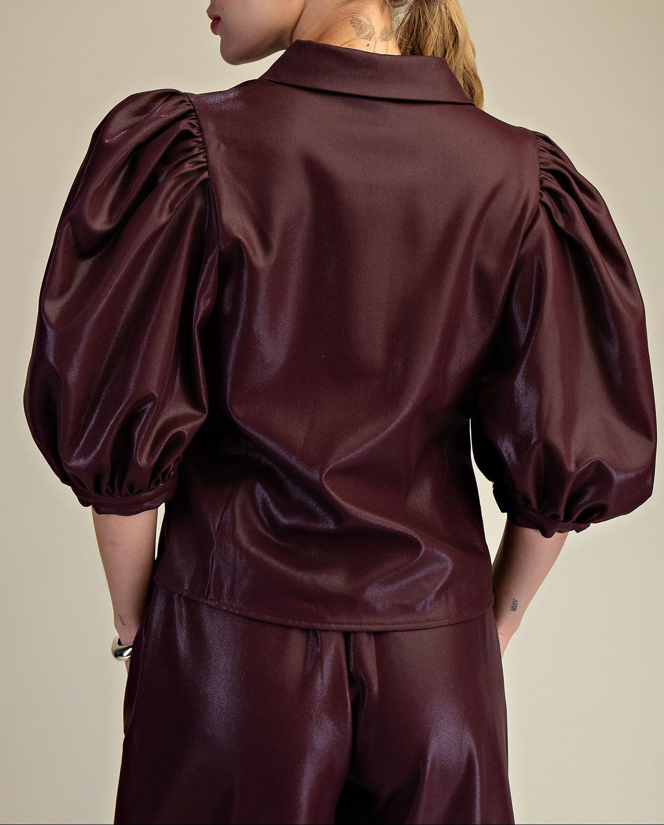 Woman wearing a burgundy faux leather outfit with puffed sleeves on a beige background