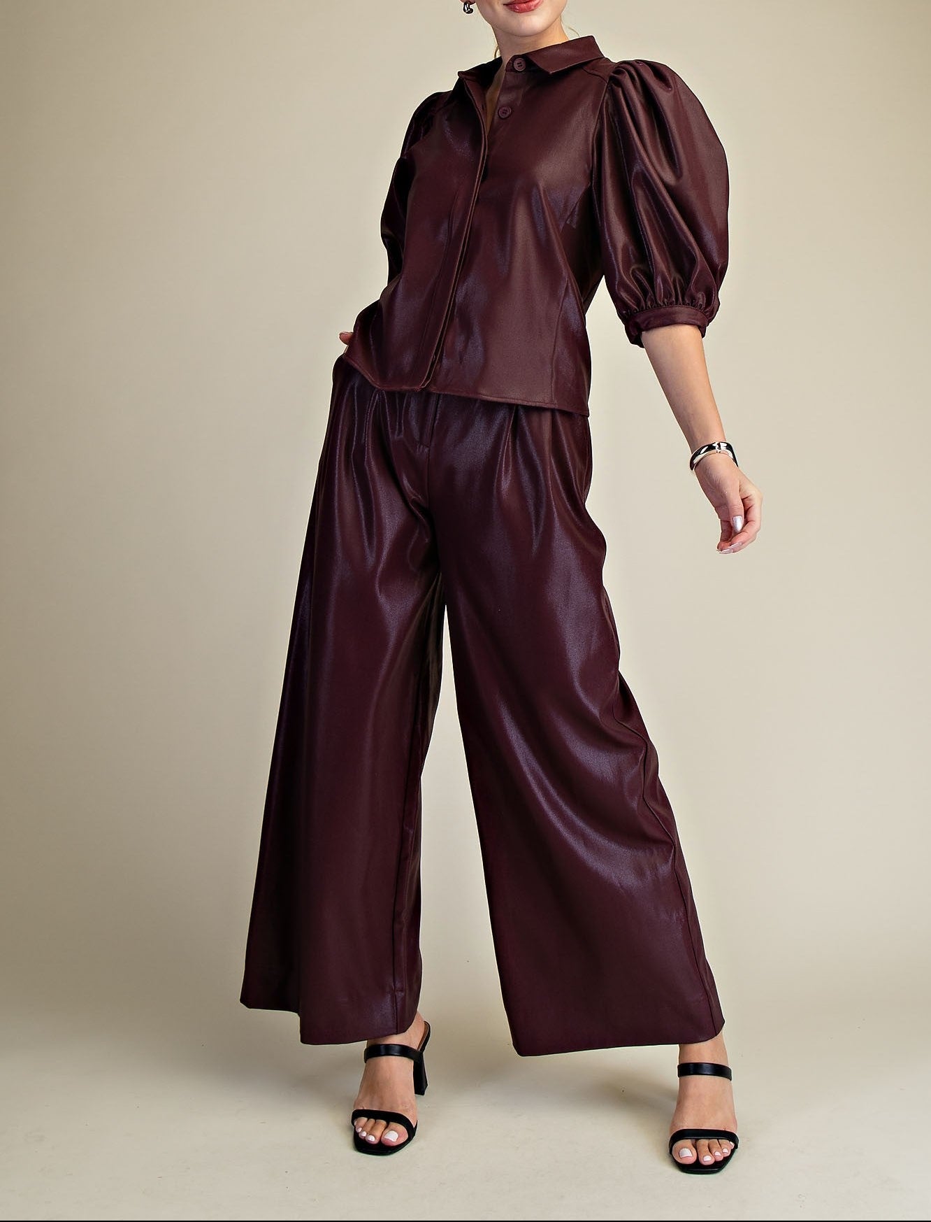 Woman wearing a burgundy faux leather outfit with wide-leg pants on a beige background
