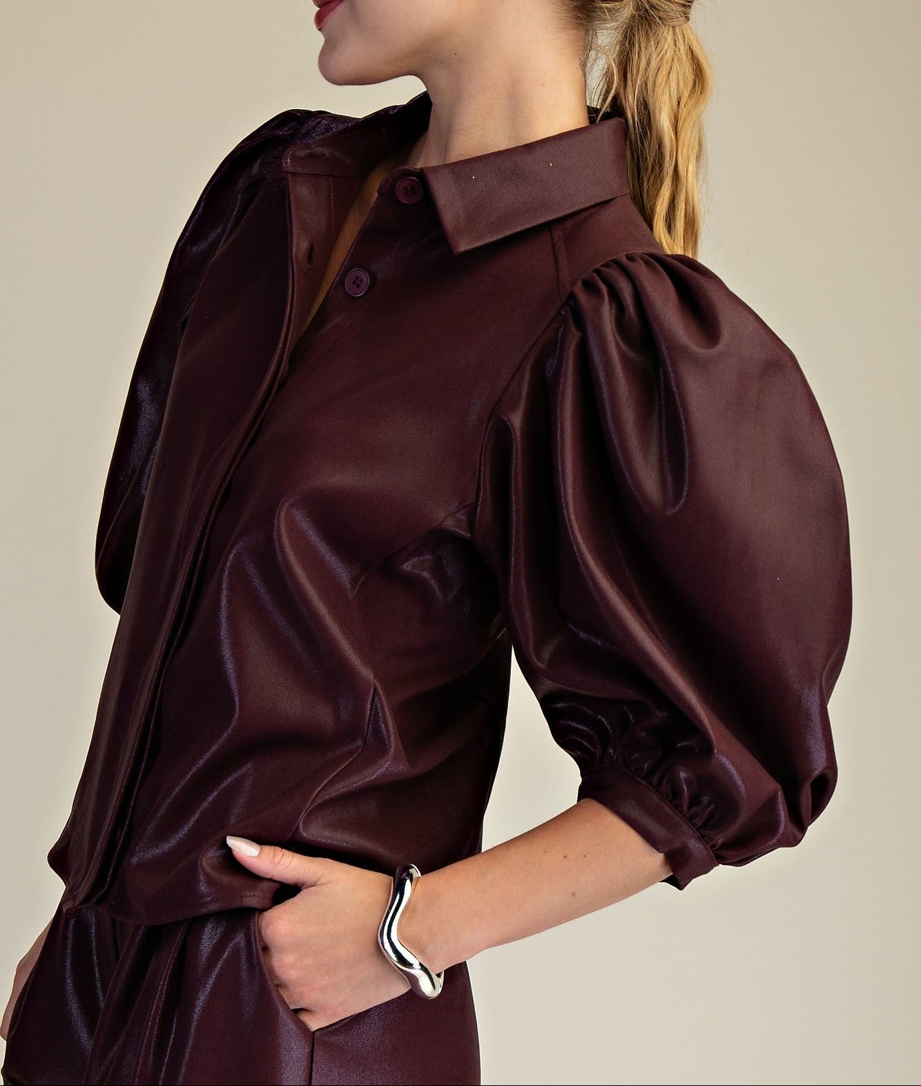 Woman wearing a burgundy faux leather blouse with puffed sleeves against a neutral background