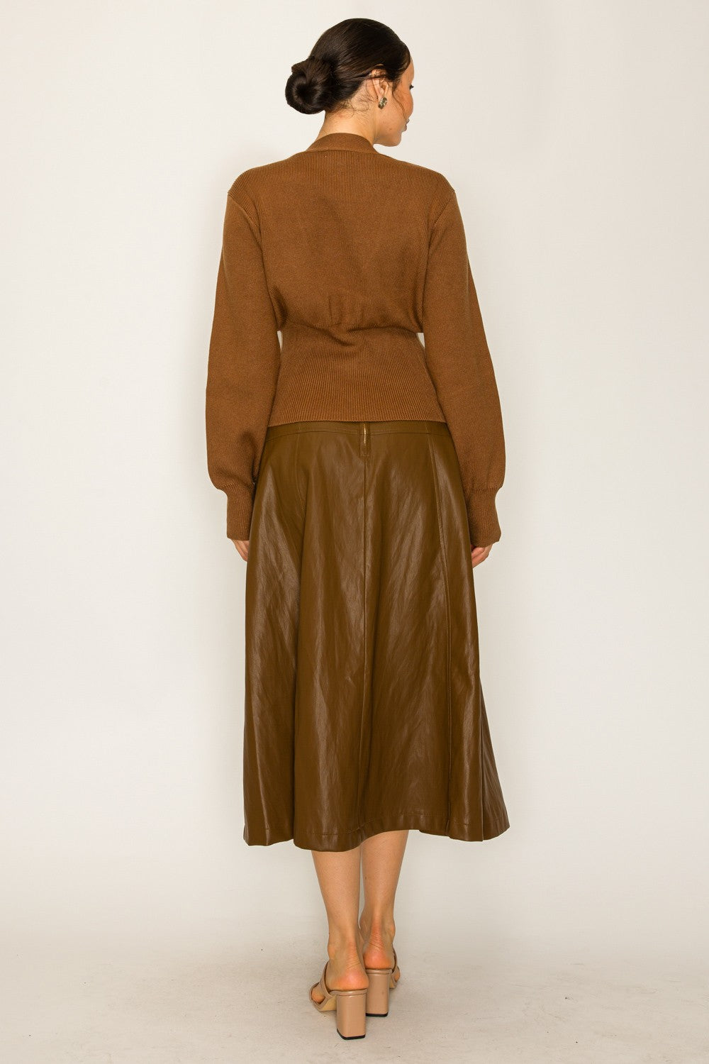 Woman wearing a brown cardigan and leather skirt on a white background