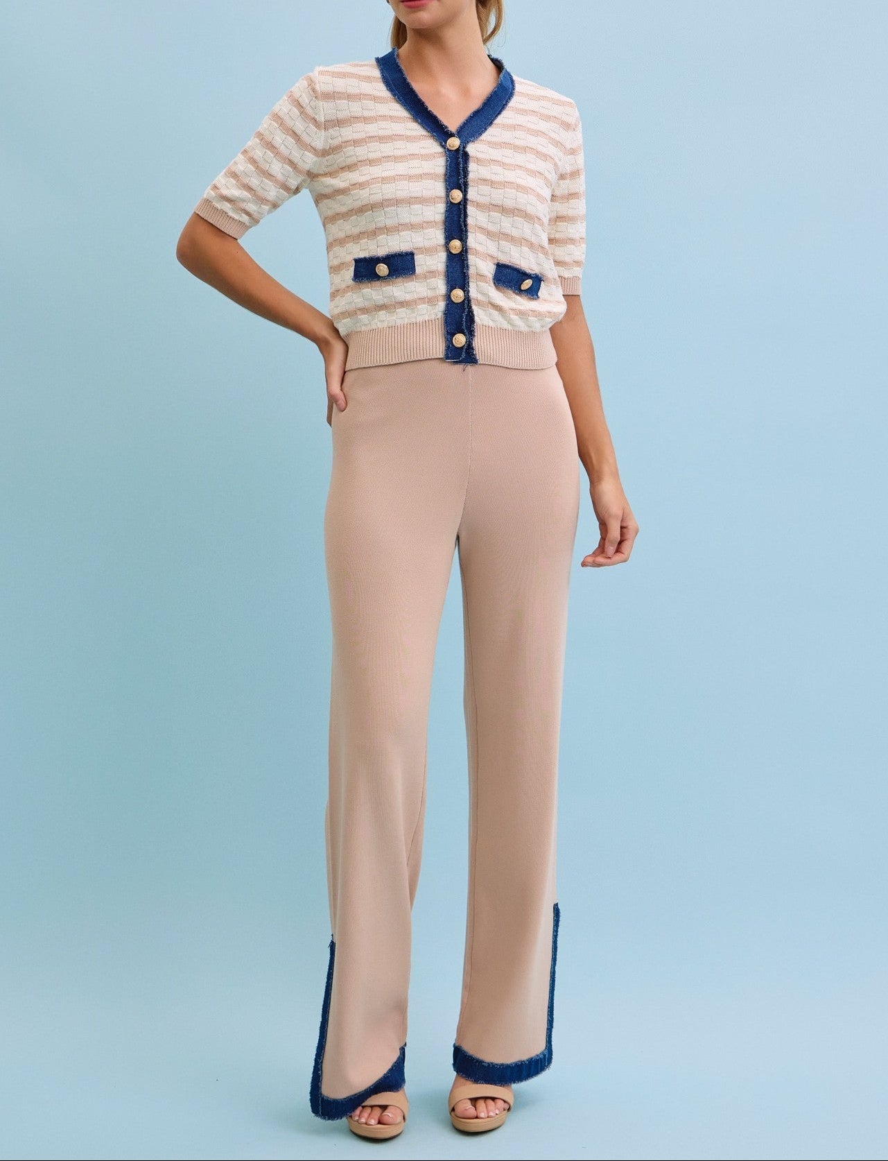 Woman wearing a beige cardigan with blue accents and matching pants on a light blue background