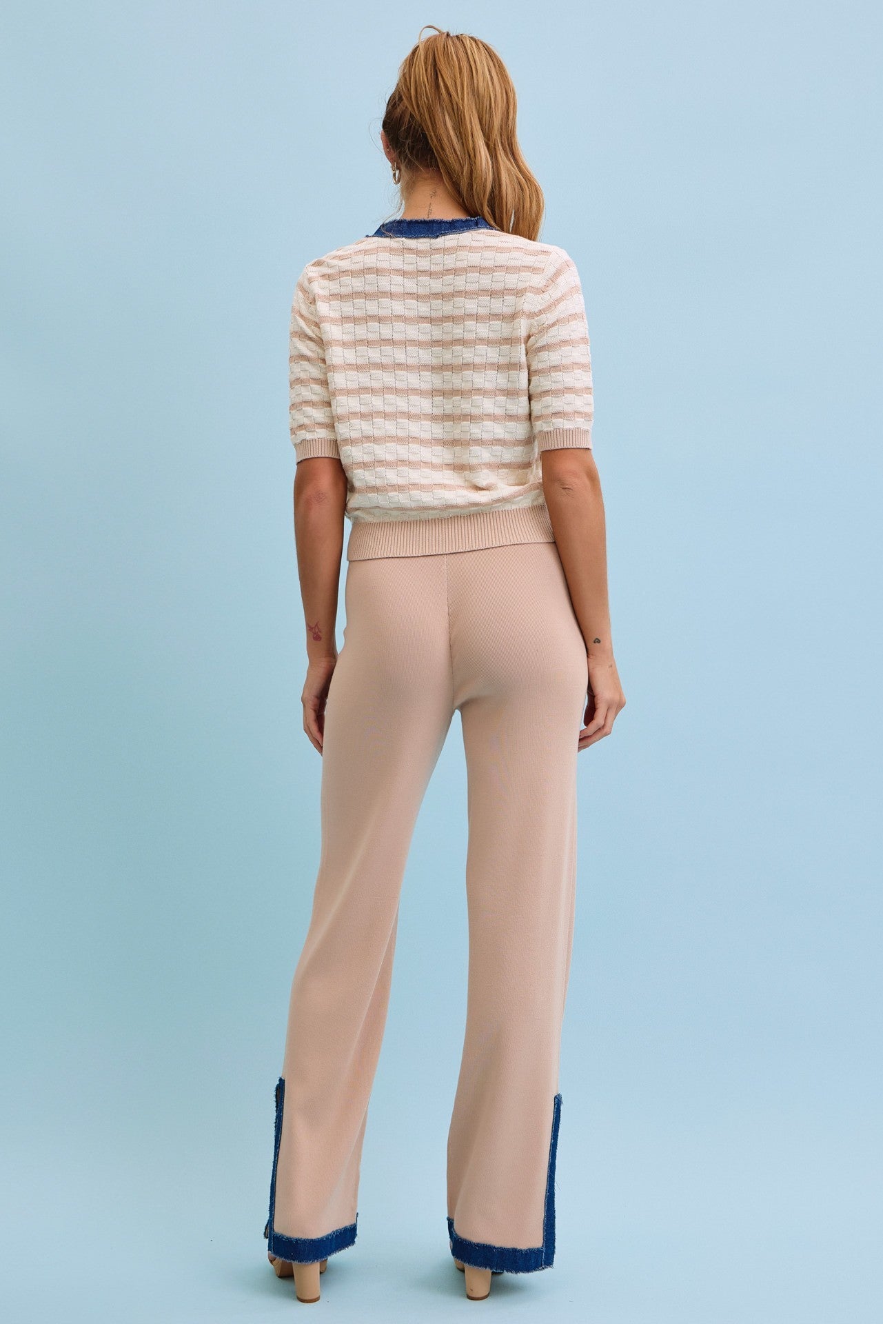 Woman wearing a striped sweater and beige pants with blue trim on a light blue background