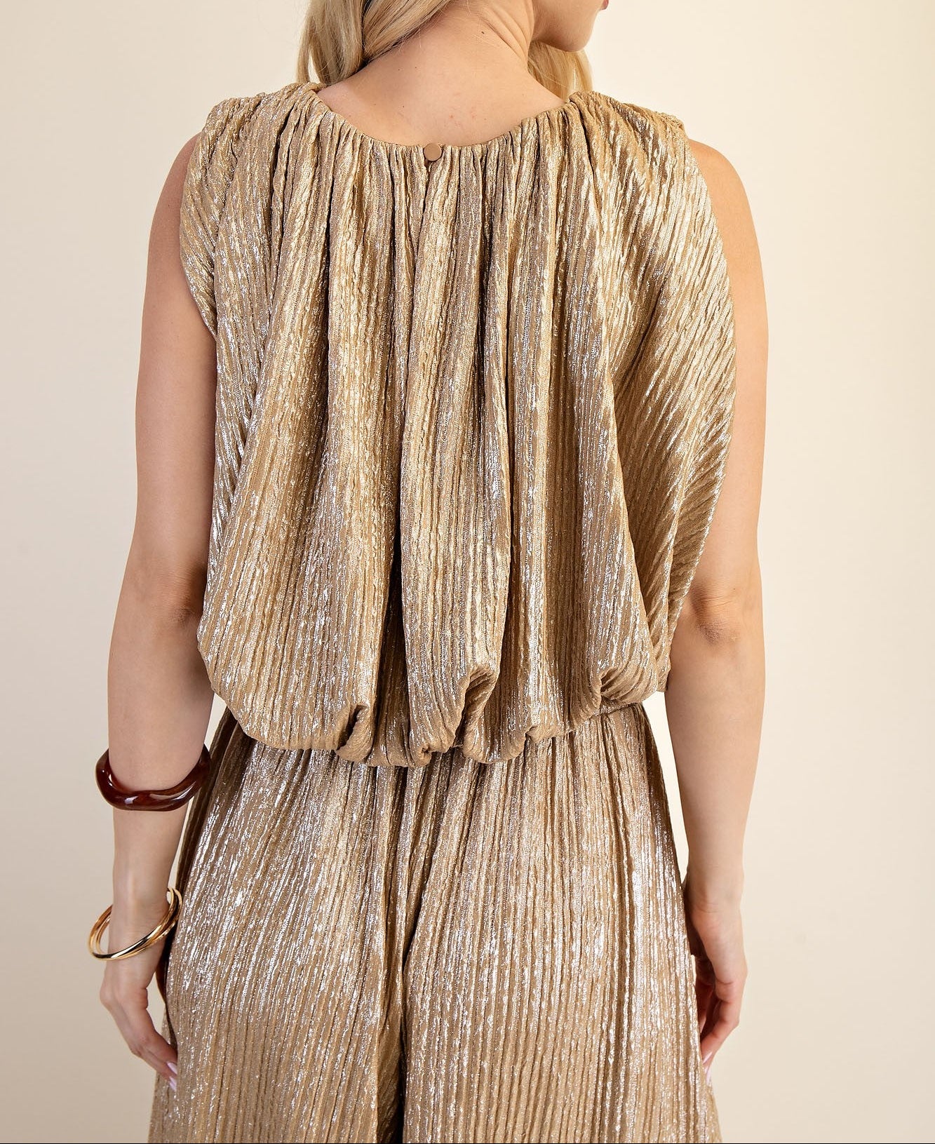 Woman wearing a gold pleated dress against a beige background