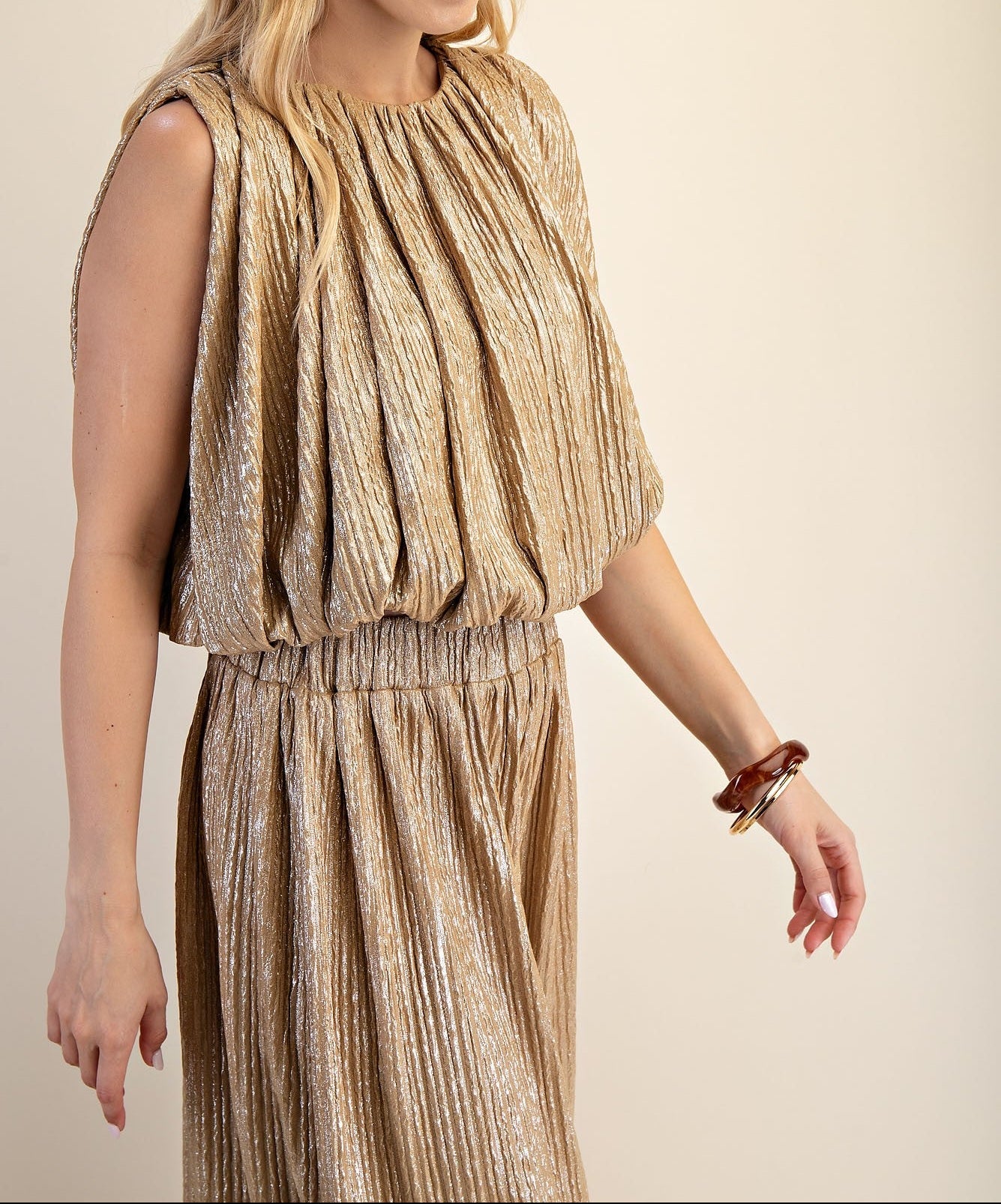 Woman wearing a gold pleated dress against a beige background