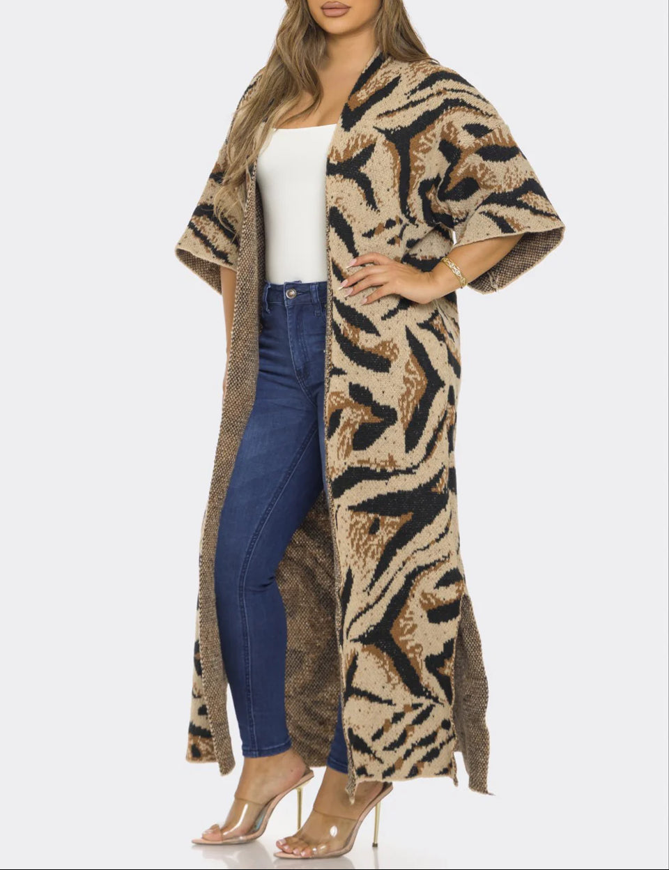 Woman wearing a long, patterned coat over a white top and blue jeans on a white background