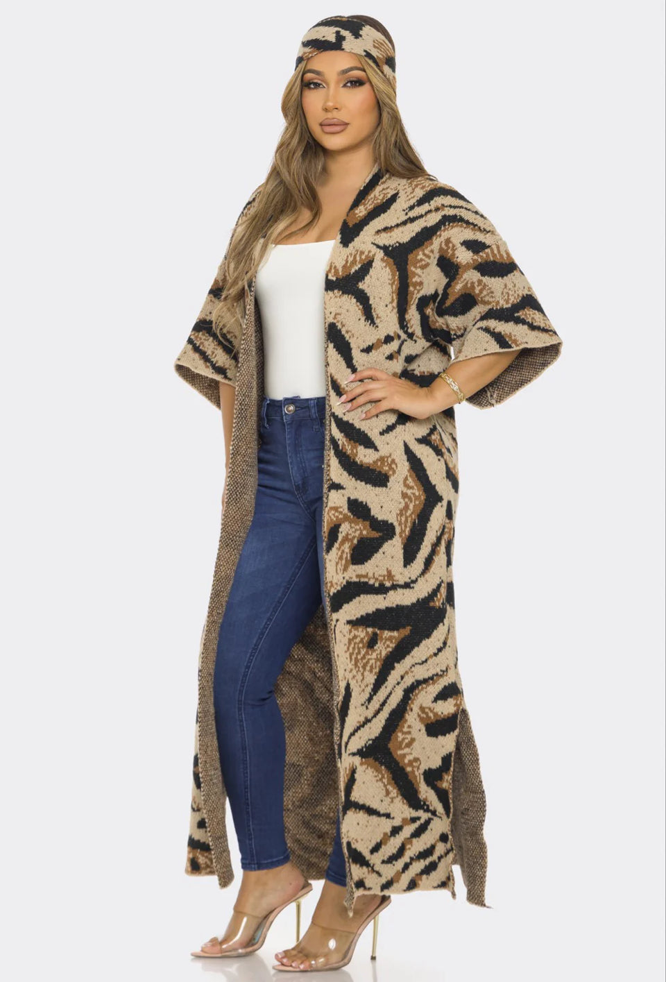 Woman wearing a long, patterned coat over a white top and blue jeans on a white background