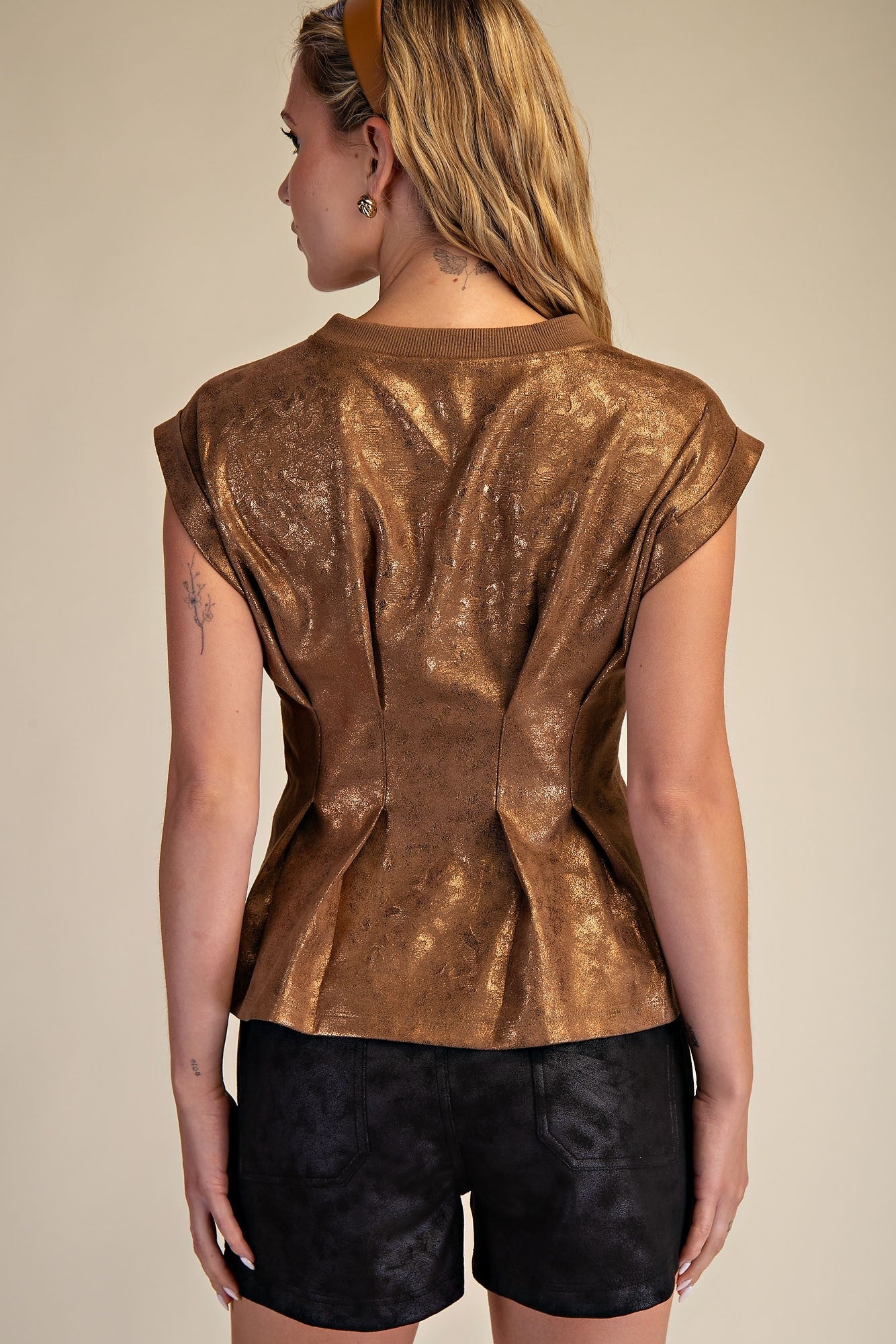 Person wearing a bronze metallic top and black shorts against a beige background
