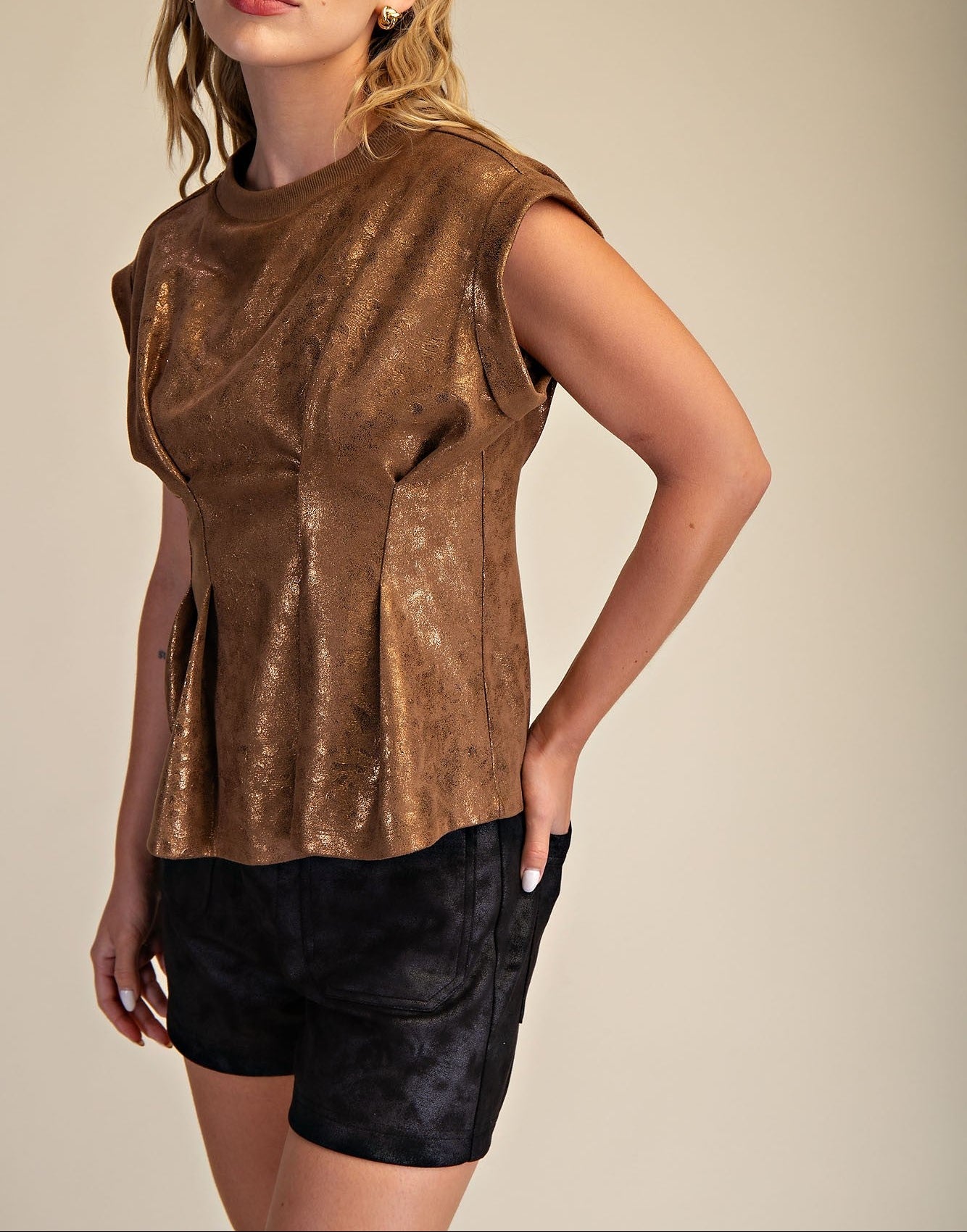 Woman wearing a bronze sleeveless top and black shorts on a beige background