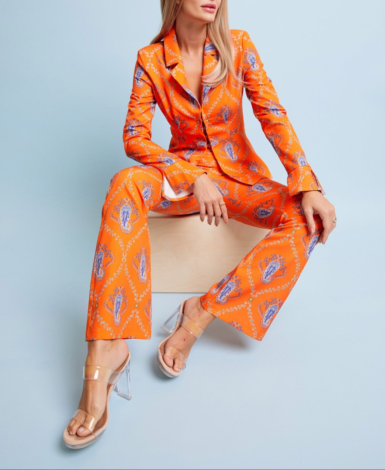 Woman in an orange patterned suit sitting on a chair against a light blue background
