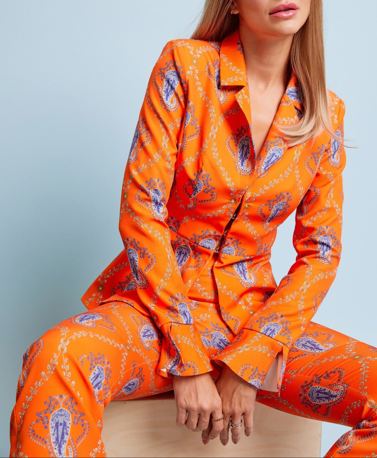 Woman wearing an orange patterned suit sitting against a light blue background